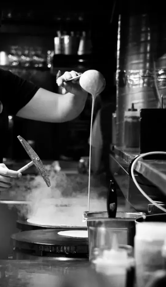 Crêpier qui étale la pâte au râteau sur le billig